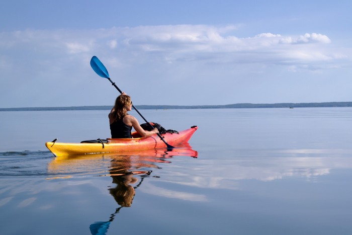 Kvinna paddlar kajak på sjön Hjälmaren. Vattnet är spegelblankt. 
